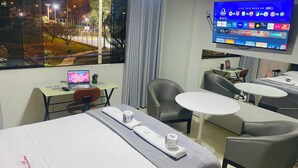 Habitación de hotel con cama, un escritorio con una computadora portátil, televisor montado en la pared y vista a la calle.