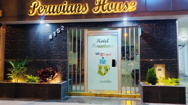 Fachada del hotel Peruvians House con un letrero de neón, una puerta de cristal con pegatinas y una escultura de pájaro.