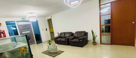 Una sala de estar moderna con una mesa de centro de vidrio, dos sofás de cuero, un acuario y una puerta de madera.