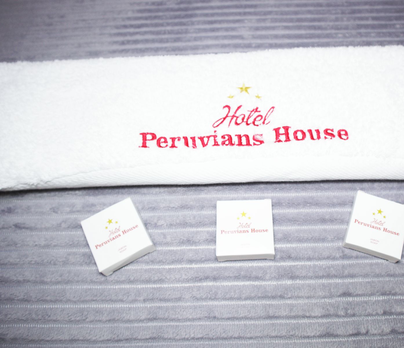 A hotel towel with 'Hotel Peruvians House' printed in red. Three small cards with the same logo are placed below the towel.