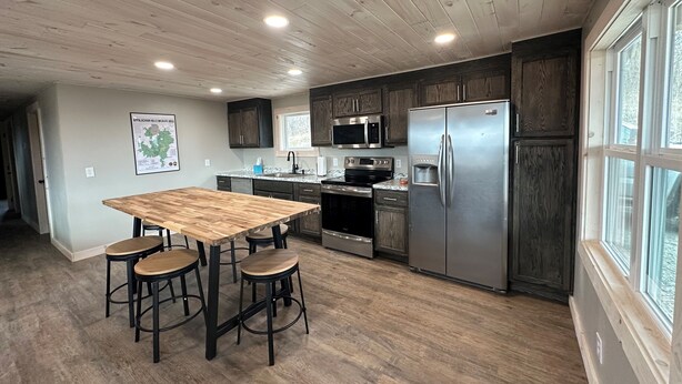 Une cuisine moderne avec des meubles en bois, des appareils électroménagers en acier inoxydable et une grande table en bois accompagnée de tabourets.