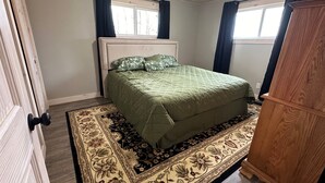 Une chambre à coucher avec un lit, une armoire en bois, une fenêtre avec des rideaux et un tapis à motifs.