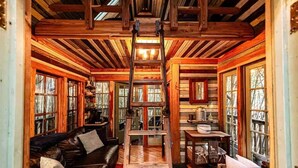 A log cabin interior with a wooden ladder, a leather sofa, a dining table, and a kitchen area. - Alpaca Treehouse in the Bamboo Forest (Atlanta)