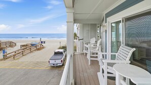 Ein Balkon mit weißen Stühlen und einem Tisch mit Blick auf einen Strand, auf dem ein Lastwagen geparkt ist.
