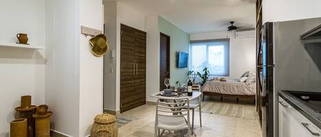 A modern kitchen with a refrigerator, a dining area with a table and chairs, and a bedroom with a bed and window.