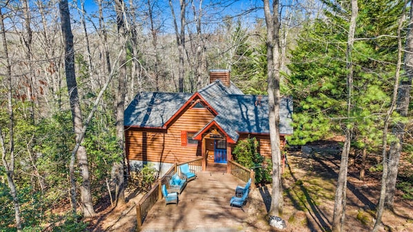 A log cabin with a porch and outdoor seating area surrounded by trees.