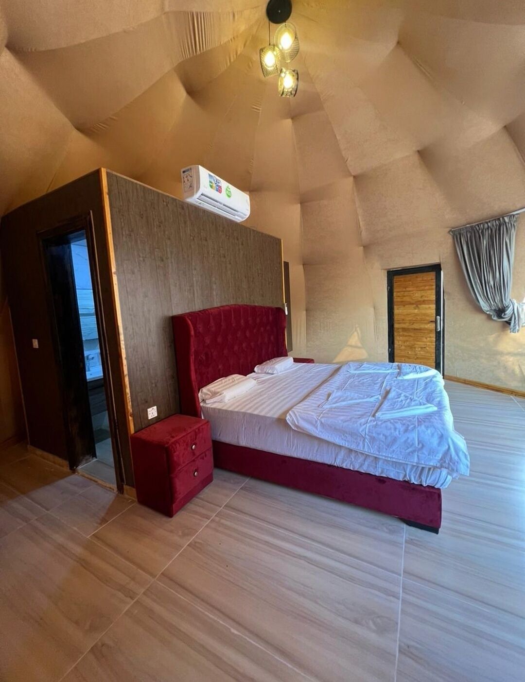 Un dormitorio con una cama, una mesita de noche roja, una puerta de madera y un ventilador de techo.
