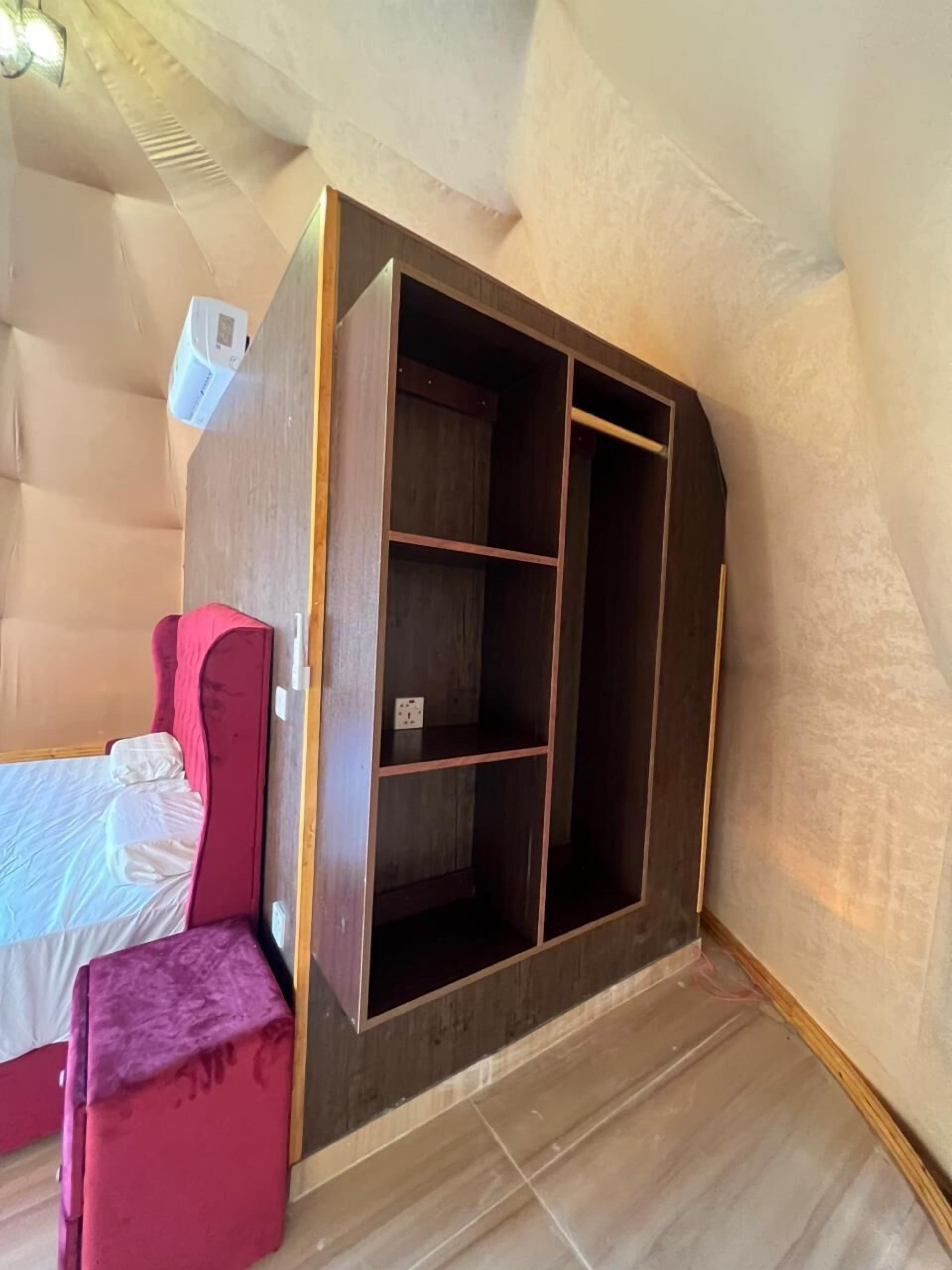 Quarto com uma cama, uma cadeira rosa e um guarda-roupa de madeira com vários compartimentos.