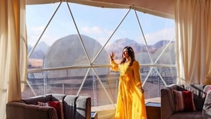 Quarto com uma janela grande, dois sofás e uma pessoa de vestido amarelo.