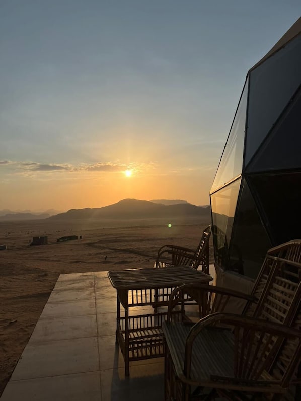 A sunset view from a balcony with a seating area and a glass enclosure.