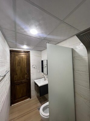 A bathroom with a wooden door, a white sink, a mirror, and a toilet. - Wadi Rum Mars Camp  (Wadi Rum)