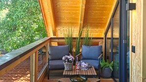 Una terraza de madera con puerta de vidrio, sofás grises, una mesa con un cuenco de cristal y una cesta de flores.