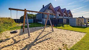 A residential area with a swing set, a sandy play area, and a modern house with a pitched roof.