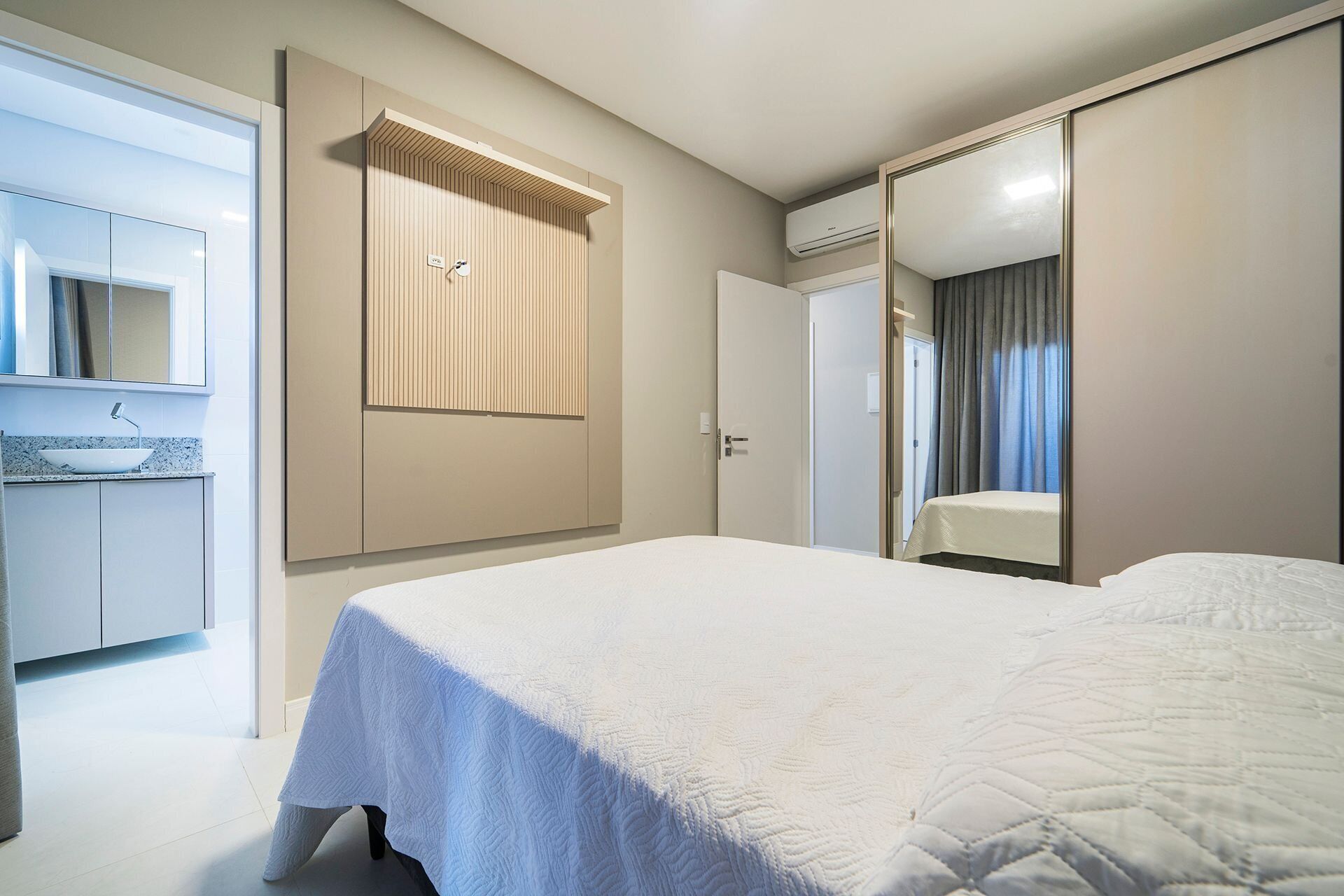 A hotel room with a bed, a bathroom with a sink, and a mirror.
