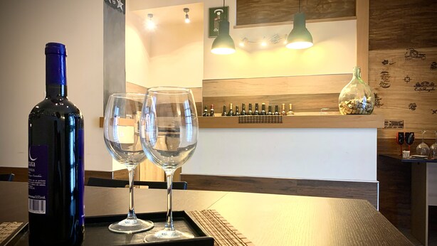 A dining area with a wooden table, two wine glasses, and a bottle of wine on a tray. - Cinema Open-space (Catania)