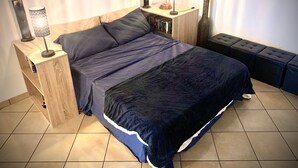 A bedroom with a bed, bedside tables, a lamp, a decorative vase, and a wall with artwork. - Cinema Open-space (Catania)