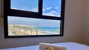 Ett hotellrum med en säng, ett fönster med utsikt över en strand och stadens silhuett.