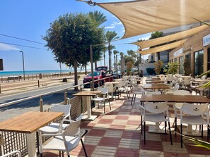 Relax by the beach at La Barraca, where tables and chairs are shaded under a large canopy.