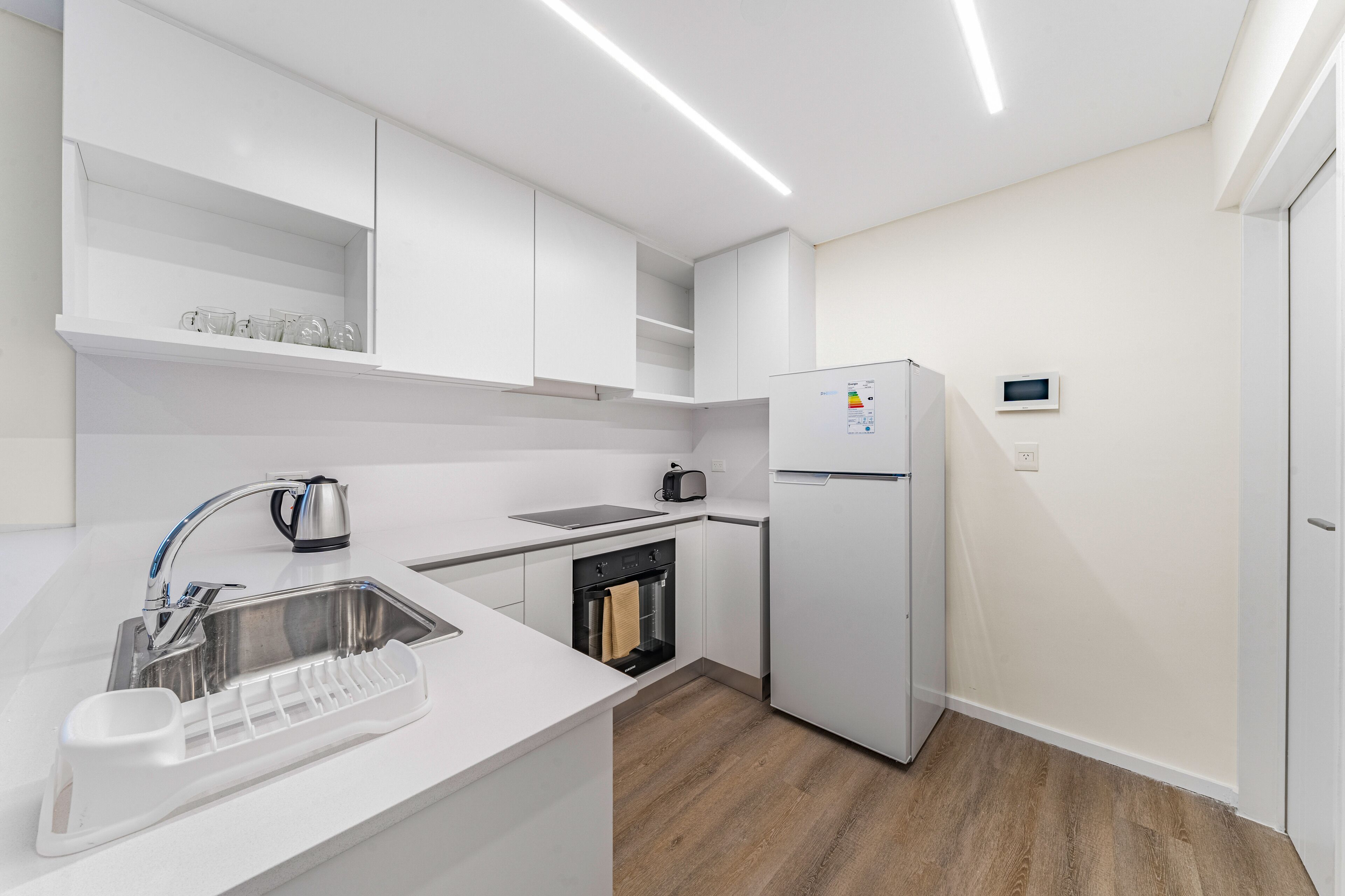A modern kitchen with white cabinetry, a stainless steel sink, a kettle, a toaster, and a built-in oven.