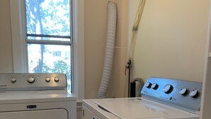 A laundry room with a Maytag washer and dryer, a window with a view of trees, and a white hose. - Clean, cozy, 1-bedroom basement apartment: 4-month rental, 2nd semester. (Toronto)