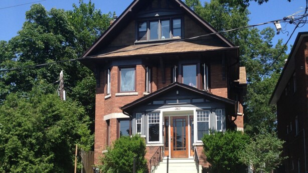 A two-story brick house with a front porch, a staircase leading to the entrance, and a well-maintained lawn with yellow flowers. - Clean, cozy, 1-bedroom basement apartment: 4-month rental, 2nd semester. (Toronto)