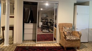 A room with a large sliding closet door, a wicker armchair, a patterned rug, and a white refrigerator. - Clean, cozy, 1-bedroom basement apartment: 4-month rental, 2nd semester. (Toronto)