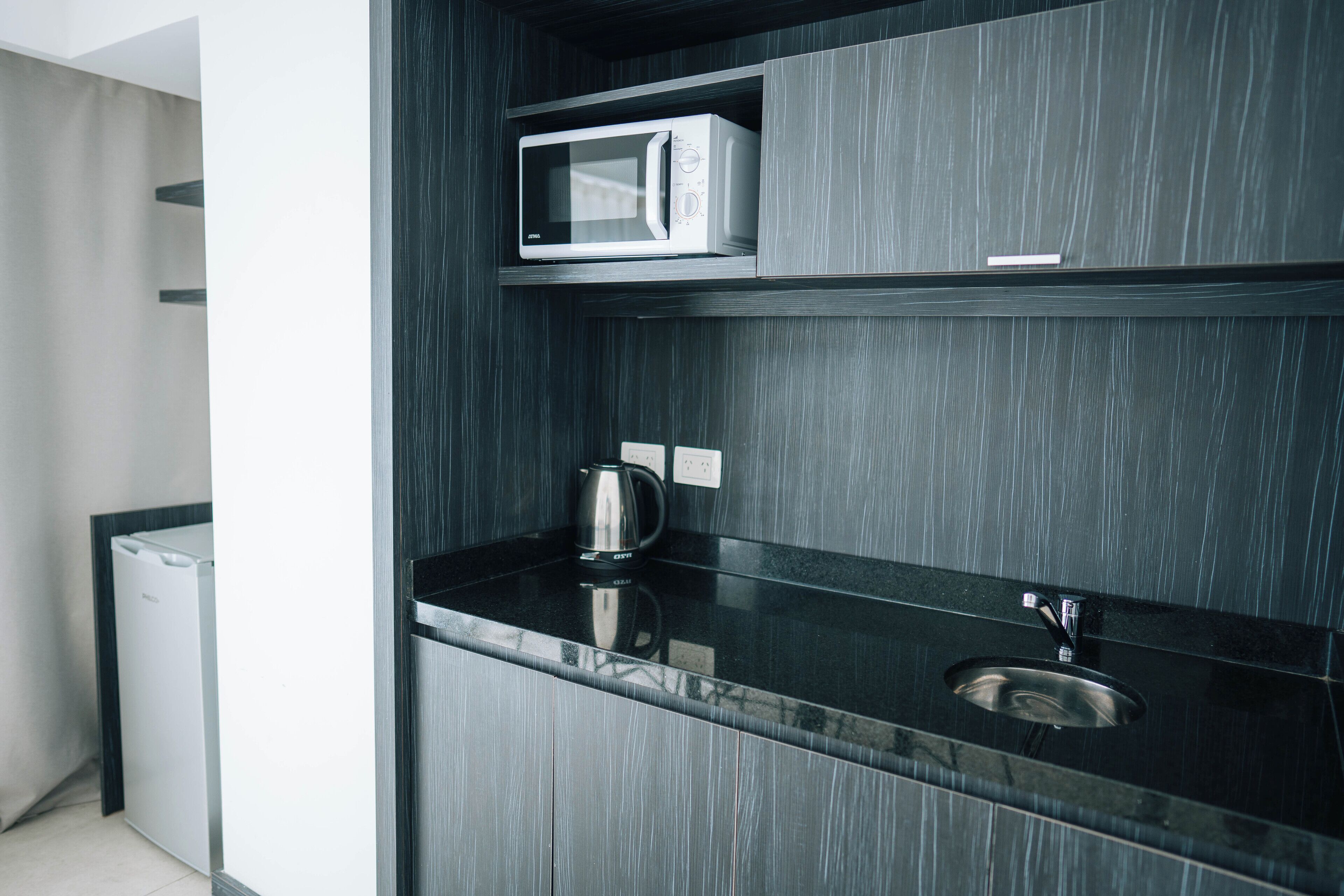 A modern kitchen with a built-in microwave, a kettle, and a stainless steel sink.