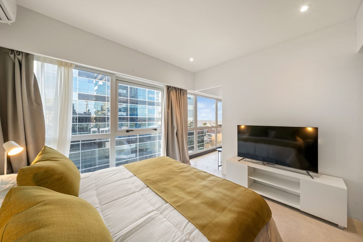 Une chambre d’hôtel moderne dotée d’un grand lit, d’une télévision à écran plat et d’un balcon offrant une vue sur la ville.