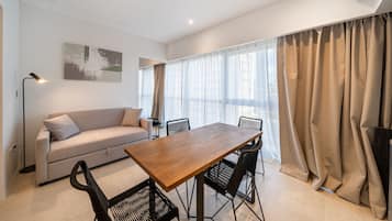 Ein modernes Wohnzimmer mit einem Holzesstisch, schwarzen Stühlen, einem beigen Sofa und einem großen Fenster mit transparenten Vorhängen.