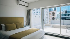A modern hotel room with a large bed, a view of the city through a sliding glass door, and an air conditioning unit on the wall. - La Vie Suite Madero (Buenos Aires)