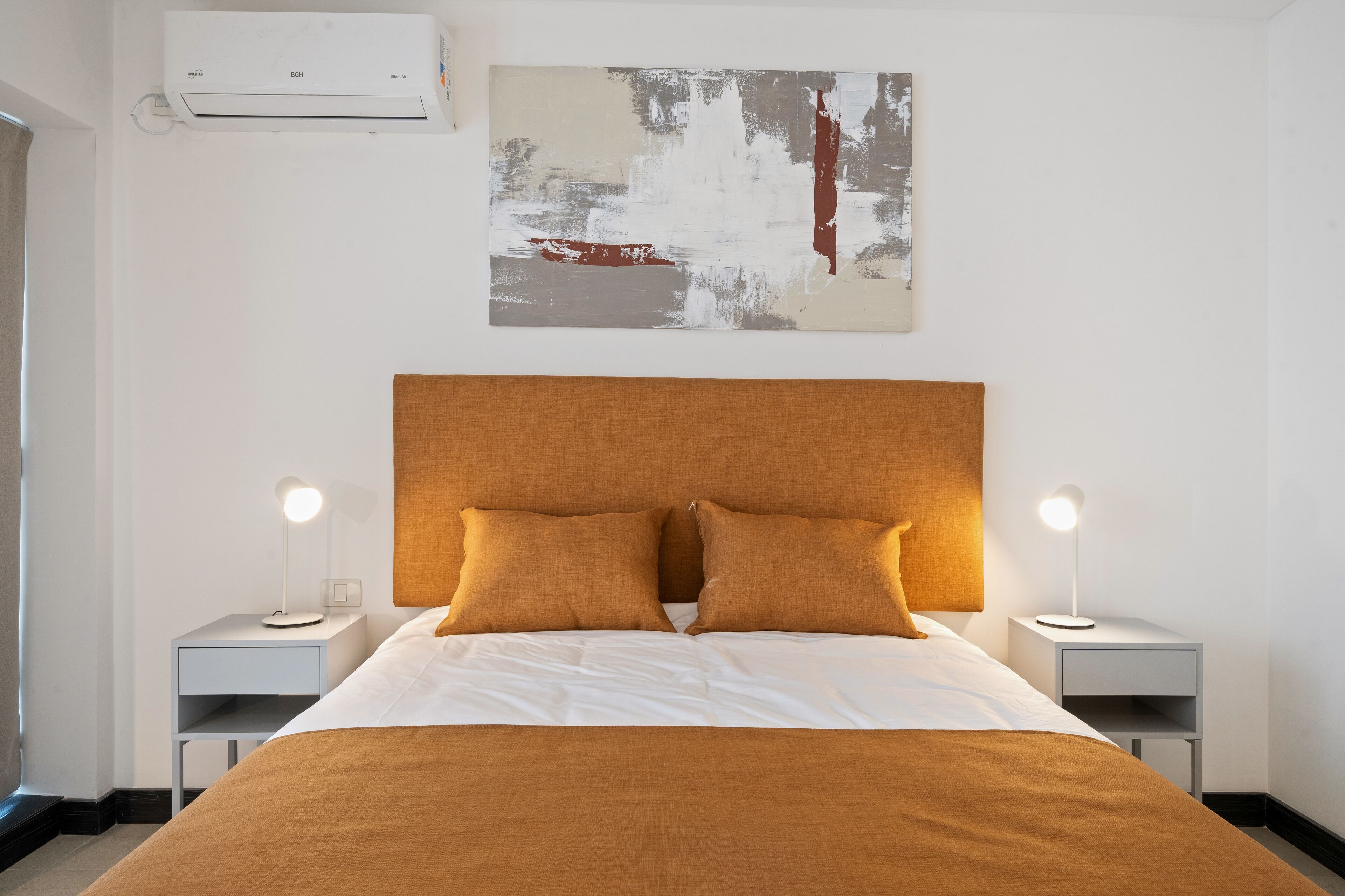 A neatly made bed with a wooden headboard, two bedside tables with lamps, and a large abstract painting on the wall.