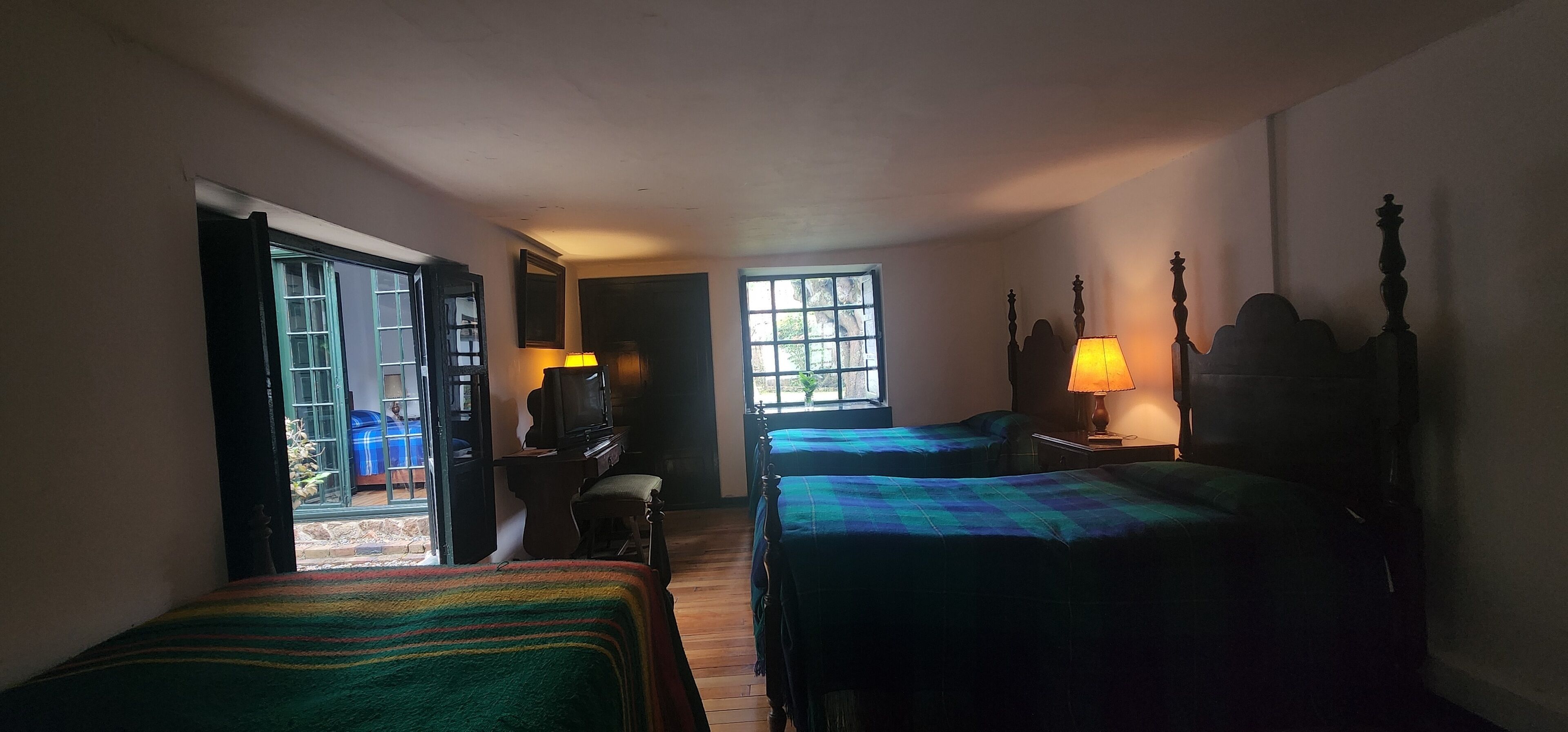 A room with two beds, a desk, and a chair. There are two windows providing natural light.