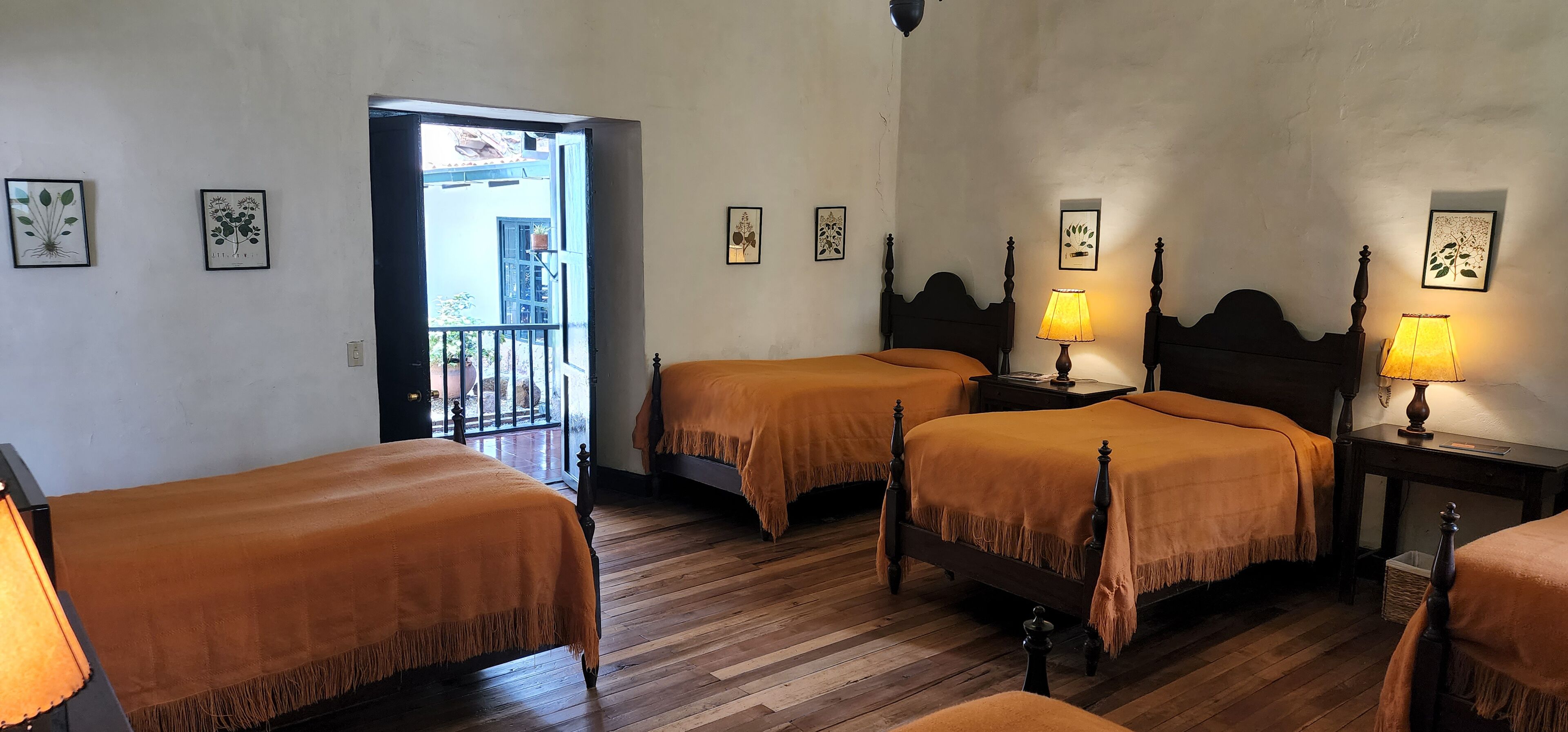 A hotel room with two beds, wooden flooring, and framed artwork on the walls.