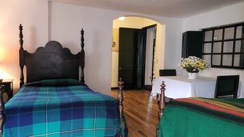 Una habitación con dos camas, una mesa con un florero, una lámpara y una ventana con contraventanas.