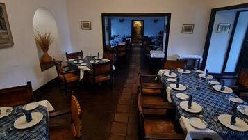 Uma longa mesa de jantar com cadeiras, um candelabro e vista para a área de refeições ao fundo.