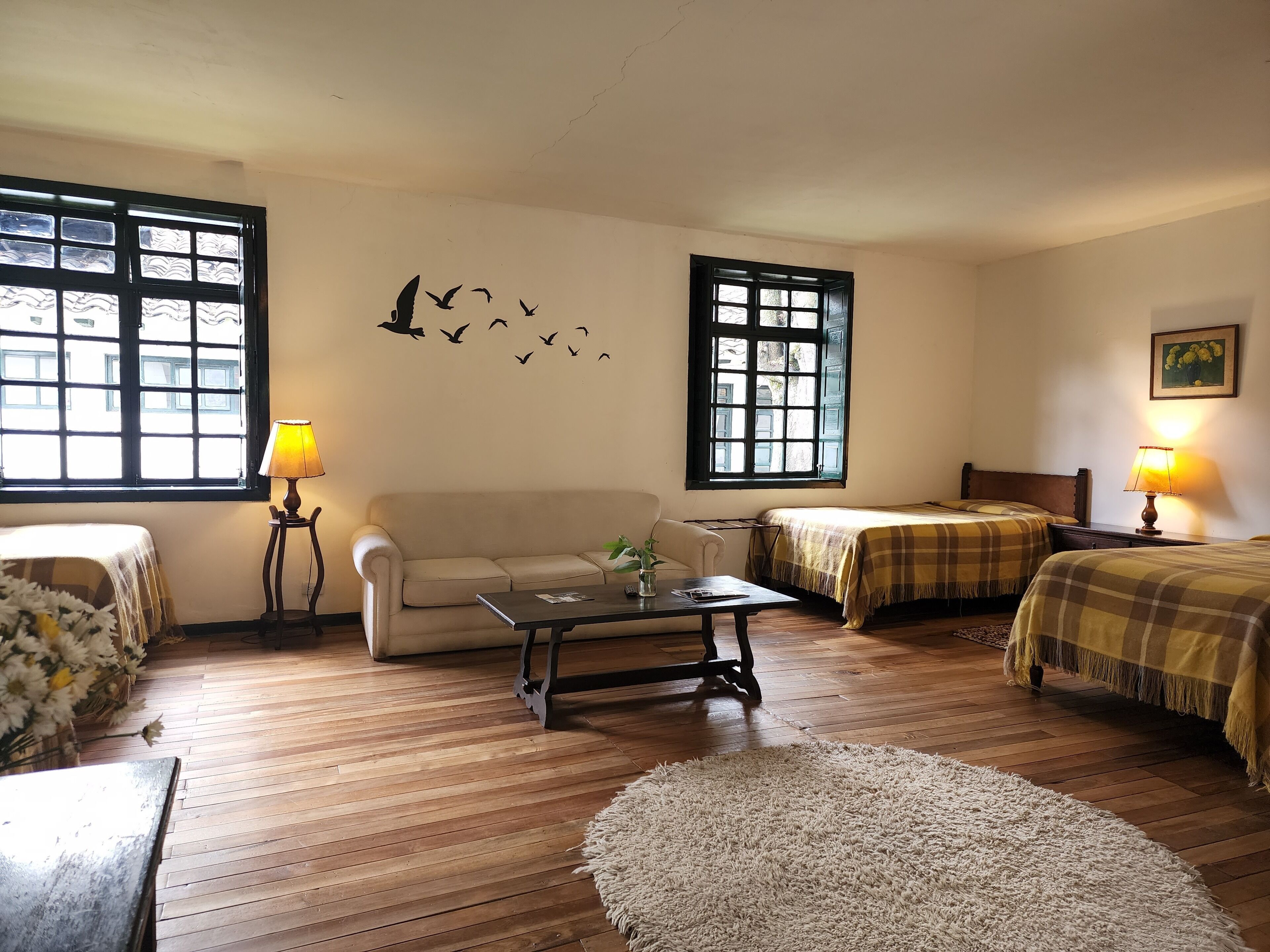A cozy room with a sofa, two beds with checkered blankets, a coffee table, and two lamps.