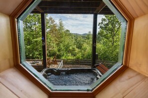 Un jacuzzi dentro de una estructura de madera hexagonal con vista a un área boscosa.