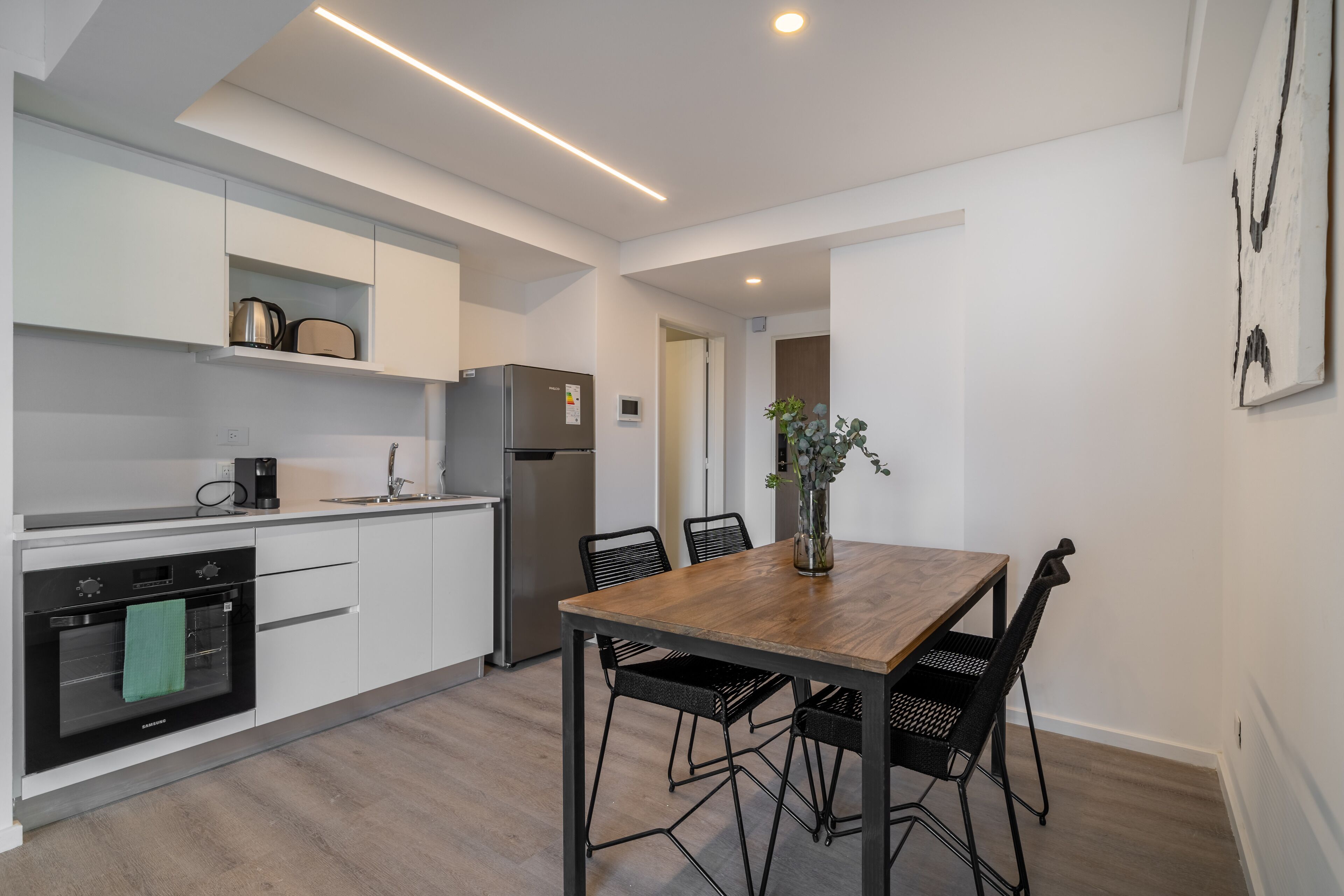 A modern kitchen with white cabinets, a wooden dining table, and black chairs.