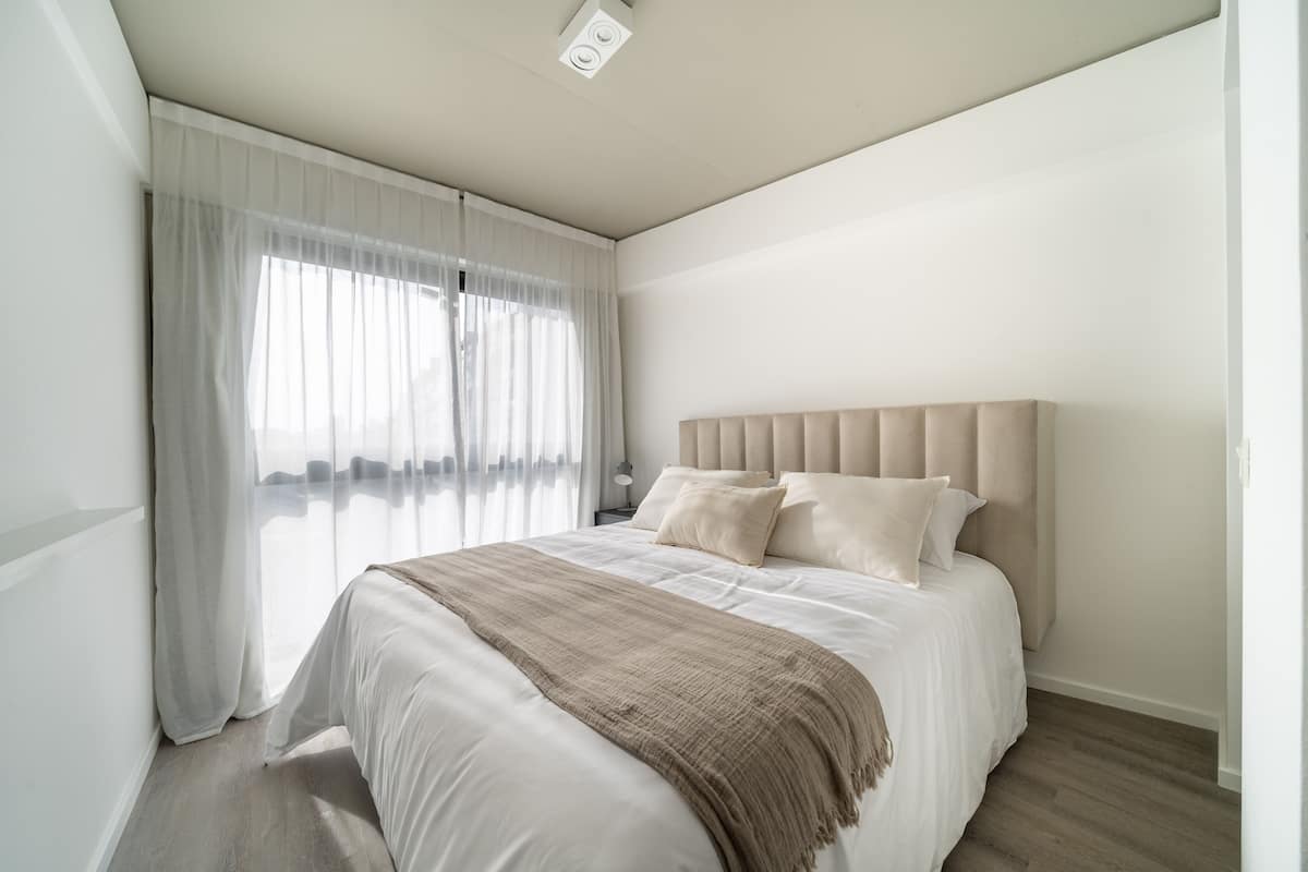 Een moderne slaapkamer met een groot bed, witte gordijnen en een neutrale kleurenpalet.