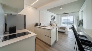 Une chambre d’hôtel moderne équipée d’une kitchenette, d’un lit, d’un bureau et d’une grande fenêtre donnant sur la ville.
