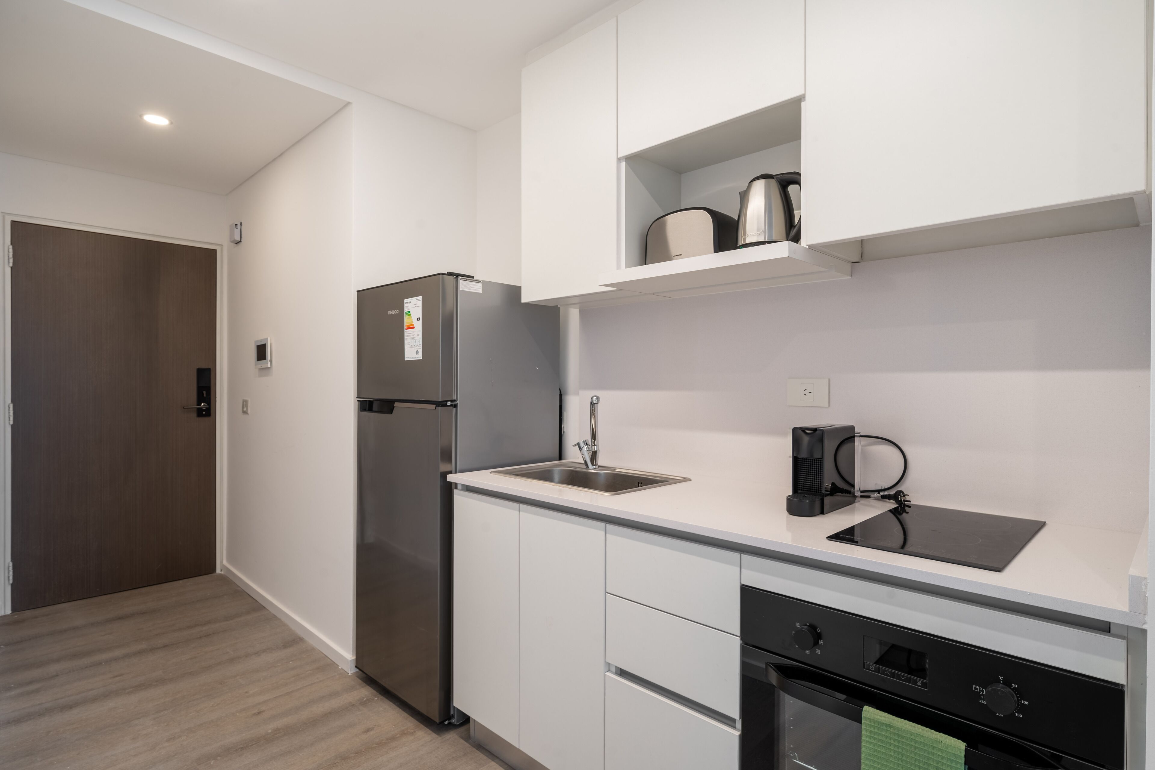 Una cucina moderna con mobili bianchi, un frigorifero in acciaio inossidabile, un forno integrato e una macchina da caffè sul piano di lavoro.
