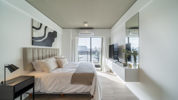 Une chambre à coucher moderne avec un grand lit, une table de chevet, un téléviseur à écran plat et une fenêtre avec des rideaux.
