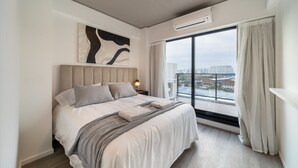 Une chambre moderne dotée d’un grand lit, offrant une vue sur la ville et équipée d’un système de climatisation.