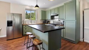 A modern kitchen with green cabinets, a stainless steel refrigerator, a central island with stools, and pendant lighting. - Wandering Pines - Scenic and peaceful getaway (Pine)