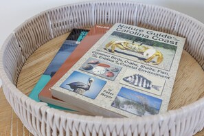 Un panier en osier contenant un livre intitulé « Guide de la nature de la côte de Caroline », de Peter Meyer, avec des illustrations d’oiseaux, de crabes, de coquillages et de paysages côtiers.