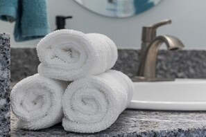 Une pile de serviettes blanches est posée sur un plan de travail en granit, à côté d’un évier avec un robinet.