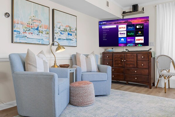 Un salon comprenant deux fauteuils, un meuble en bois, un téléviseur diffusant des services de streaming et deux tableaux accrochés au mur.