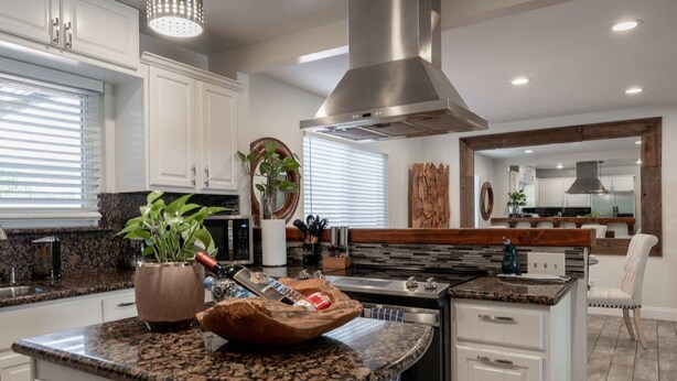 A modern kitchen with granite countertops, white cabinetry, a stainless steel range hood, and a central island with a sink. - Charming Coastal Home – Carmel, Pebble Beach & Big Sur STR25-000020 (Marina)