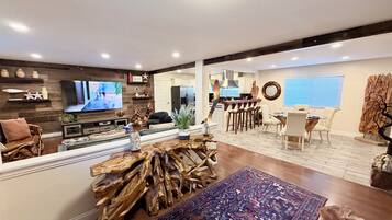 Un vaste espace de vie comprenant un téléviseur, un décor en bois, une table à manger et une cuisine à l’arrière-plan.