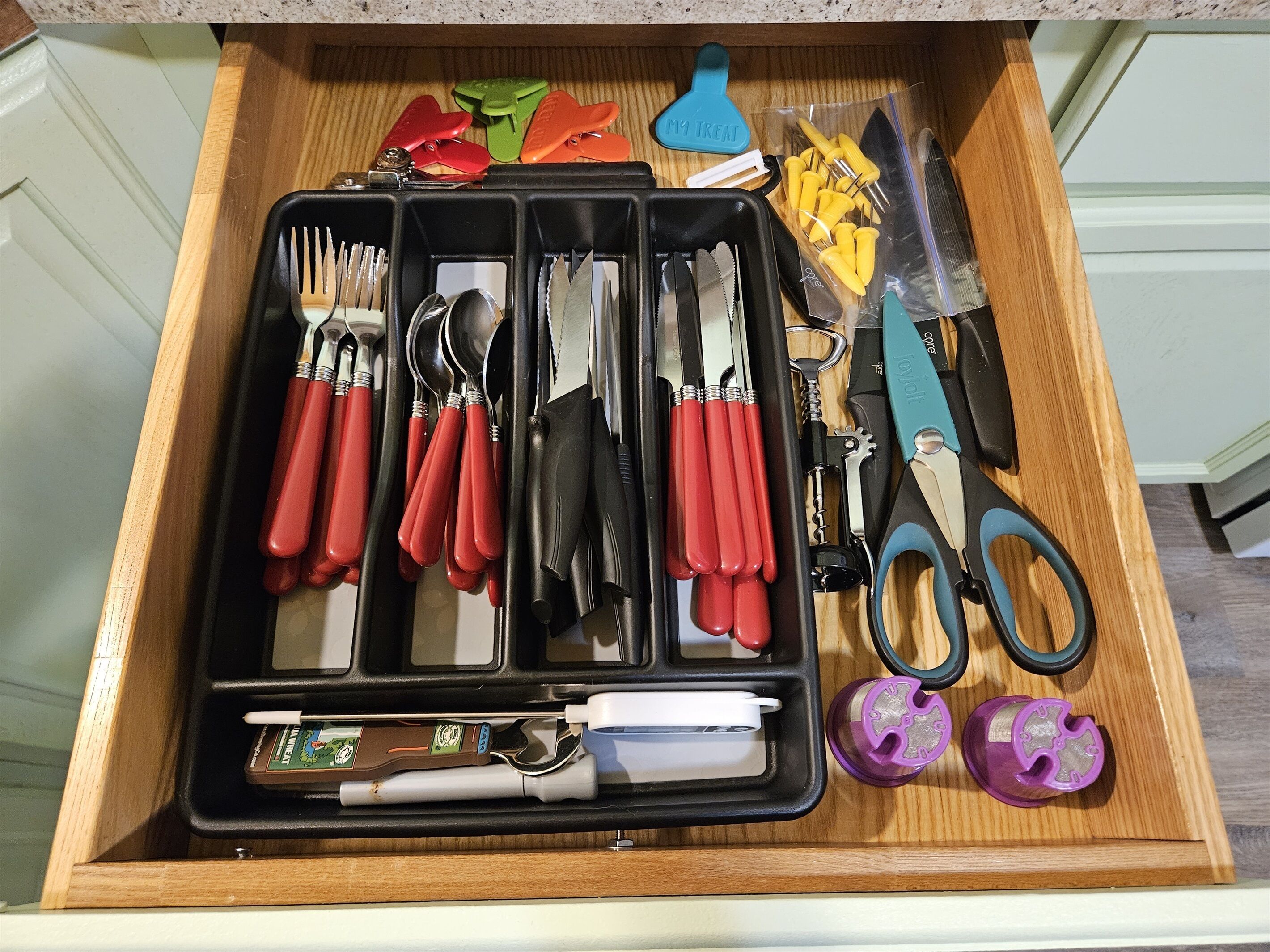 A drawer containing various kitchen utensils and tools, including knives, spoons, and a can opener.